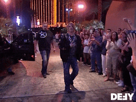 Reality TV gif. Criss Angel on Mindfreak walks next to a crowd of clapping people as someone video tapes him. Criss Angel makes a circle motion with both his hands next to his head and says, “This is loco.”