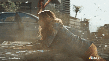 TV gif. Natalie Zea as Eve on La Brea falls off of a ledge into a chasm that has opened up in the city road. A woman's hand reaches out to hers and grabs her wrist as she falls. 