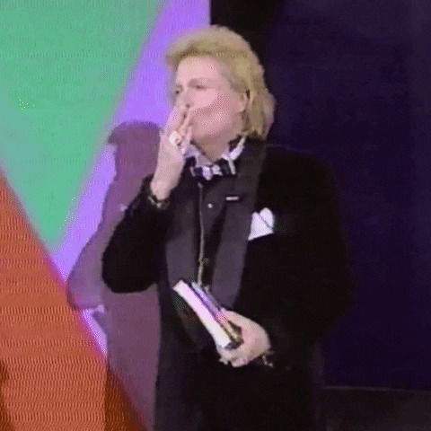 Video gif. Walter Mercado blows a kiss out to the audience while holding a book, and turns to leave.