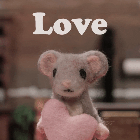 Cartoon gif. Stop motion light brown felted mouse holds up a pink heart to its chin, shaking its head in a delighted manner. Text, "Love."