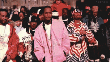 Video gif. A group of swagged out men are walking slow motion down the street intimidatingly. 