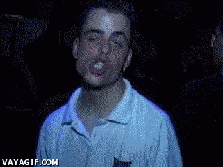 Video gif. A drunk man with droopy eyelids and lips flared open leans toward us as lights flash and a DJ plays in the background.