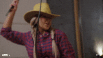 Reality TV gif. Cathy on Married at First Sight, wearing a cropped plaid button-down shirt and a cowboy hat, flings a whip and acts like she's riding a horse.