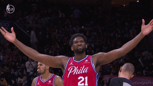 Sports gif. Joel Embiid of the Philadelphia 76ers walks across court, raising his arms to the side, scrunching his nose and nodding like he's feeling this moment.