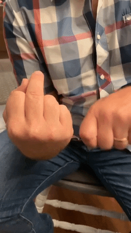 Video gif. Man gestures with his fist like he is reeling in a fishing pole, and as he does so the middle finger on his other fist slowly rises.