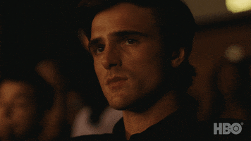 TV gif. Jacob Elordi as Nate Jacobs in Euphoria, sits among an audience and appears nervous, looking left and then bowing his head down slightly.