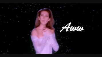 Music video gif. From "My Heart Will Go On," Celine Dion in shoulderless gown presses her hands to her heart as she sings in front of a black starry night sky. Text, "Aww."