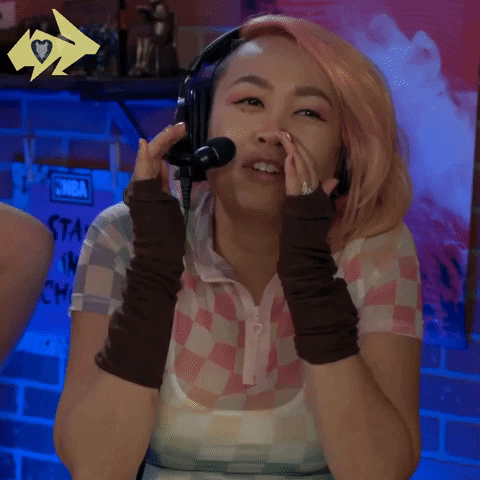 Video gif. Michelle Nguyen on Hyper RPG livestream wearing a headset and holding her hands in front of her face, smiling as she says "who dis?" which appears as text.