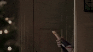 Ad gif. Max Verstappen popping into a doorway with a bottle of champagne, wearing a scarf and a suit.