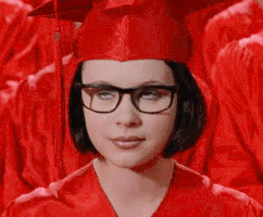 Movie gif. Thora Birch as Enid in Ghost World. She has glasses on and is wearing a red graduation cap and gown and she rolls her eyes while waiting with the other graduates.