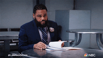 TV gif. Anthony Anderson as Detective Kevin in Law and Order. He's sitting at a desk flipping through a folder and he wordlessly points at the seat in front of him.