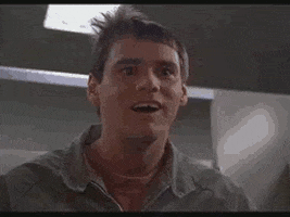 Movie gif. Jim Carrey as Lloyd in Dumb and Dumber smiles confusedly. He looks at his watch and then glances ahead as if in shocked realization. 