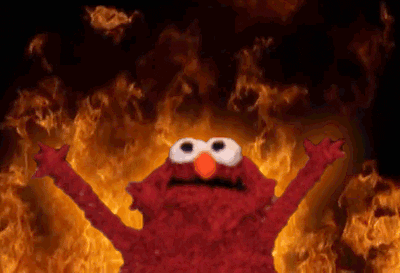Elmo from Sesame Street raises his hands as fire rages in the background. 