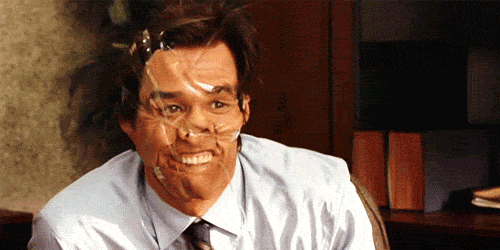 Movie gif. Jim Carrey As Carl Allen in Yes Man has covered his face in clear packaging tape, smooshing his nose down and pulling his lip up to reveal all his top teeth. He waves nonchalantly. 