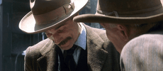 Movie gif. Daniel Day Lewis as Daniel Plainview in There Will Be Blood. He's wearing a gentleman's fedora and a suit. He chuckles as he says, "Thank you. That's very nice." to an older man standing in front of him.