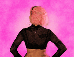 Celebrity gif. Standing with her back to us, Doja Cat turns to look over her shoulder at us, smiles, and says "hey," which appears as text.