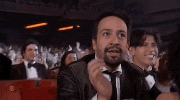 Celebrity gif. Lin Manuel Miranda at the Tony Awards, stands up in the audience, and applauds enthusiastically for someone off screen, a look of happiness and almost disbelief on his face.