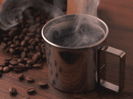 Video gif. Steam rolls out of a metal cup full of coffee next to a bag of coffee beans spilled out on the table.
