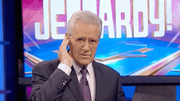 TV gif. Alex Trebek from Jeopardy has his hand to his ear as if receiving a message and he smiles and points at us, nodding and giving us a thumbs up.