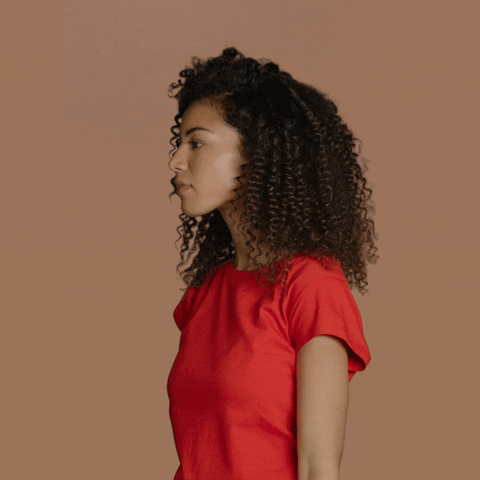 Video gif. Woman with a head of curly hair and a solid red t-shirt turns her head slowly towards us as her eyes widen and jaw drops in dramatic, repulsed shock.