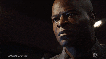 TV gif. Hisham Tawfiq as Dembe on The Blacklist has a serious, angry expression his face that changes to sudden shock 