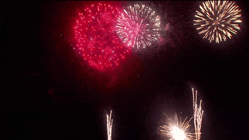 Video gif. Fireworks shoot up into a black sky, bursting into colors of red, orange, purple, and green. 