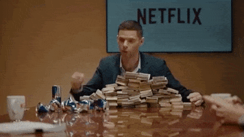SNL gif. Mikey Day sits at a conference sized table next to a pile of smashed energy drinks and a massive stack of money. He grabs the money and tosses it to others at the table. Text, "Here's money! Go!"