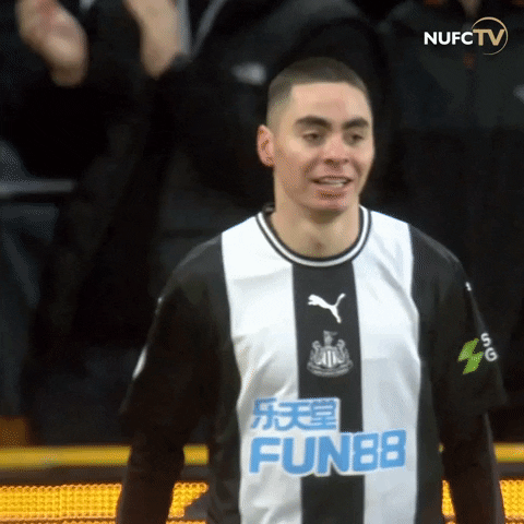 Sports gif. Miguel Almiron of Newcastle United walks across the field in a black and white Jersey, holding out a fist with a determined look on his face. Logo at the top for NUFC TV. 