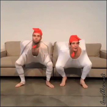 Video gif. Two men in chicken costumes bounce and bob around before flapping their wings.