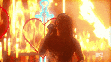 Celebrity gif. Kacey Musgraves is performing on stage at the 2021 VMAs and she hits a high note as flames fly out behind her.