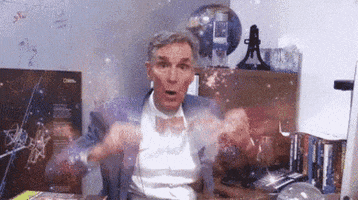 TV gif. Bill Nye is sitting at his desk and is imitating having his mind blown, exploding his hands from his mind. The universe and cosmos are overlaid in front of him, and orbs of light fly out in every direction.