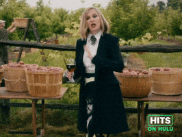 Sponsored GIF. Catherine O'Hara stands outside in front of an apple orchard, formally dressed with a glass of red wine in hand. She leans back and places her other hand on hip and says “Cheers, to you Mom!” with a charming smile.