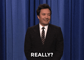 Tonight Show gif. Jimmy Fallon stands in front of the curtain and looks doubtful, smiling and saying, "Really?!" while looking to the side for confirmation. 