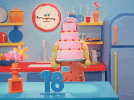 Video gif. Woman wearing a lavender wig with pigtails and a yellow shirt. She's standing in a cartoon-themed kitchen lowering a multi-tiered pink birthday cake from in front of her face next to a sign that reads, "Happy 18th."