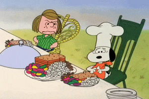 Peanuts gif. Snoopy, seated at a table with Peppermint Patty, pulls a chef's hat down over his eyes, embarrassed. In front of the two sits plates full of a strange combination of food, including white bread, popcorn, cinnamon sticks, and jelly beans. Patty looks over at Snoopy angrily, her hands on her hips.