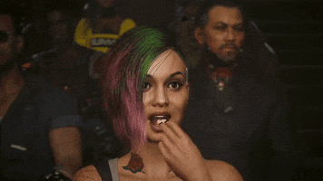 Video game gif. Judy Alvarez in "Cyberpunk 2077" smiles and pops a piece of popcorn in her mouth, looking out with an interested expression from the audience of a theater. 