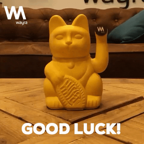 Video gif. A yellow Japanese Lucky cat statue sits on a coffee table. Its paw moves up and down. Text, “Good luck!”