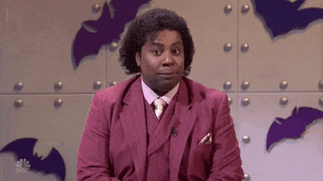 SNL gif. Kenan Thompson dressed in a fancy suit sits in a room with bat cut outs behind him. Something that he heard catches him off guard. He looks away awkwardly while gasping a little, and his eyes go wide with shock. He looks back with an amused look on his face. 