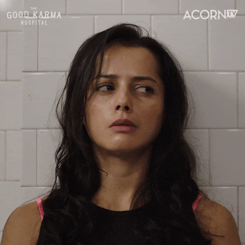 TV gif. Amrita Achara as Ruby Walker in Good Karma Hospital looks dejected and worn out, with her back against a tiled white wall, leaning her head forward and pinching the bridge of her nose.