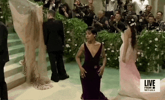 Met Gala 2024 gif. Kerry Washington, in a maroon velvet gown with a structured plunging neckline that frames her face, poses for the cameras, mugging moodily, landing with her hand elegantly primping the nape of her neck.