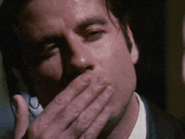 Movie gif. Close up on John Travolta as Vincent Vega in Pulp Fiction as he blows a kiss with a seductive gaze.