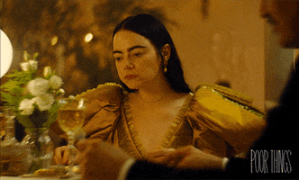 Movie gif. Emma Stone as Bella in Poor Things. She's sitting at a table in a big yellow gown and she's disgusted by the food she's chewing. She unhesitatingly spits out her food back onto her plate.