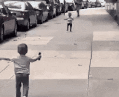 Video gif. Two small boys, about three or four years old, run to each other on a sidewalk, arms spread wide and embrace.