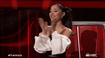 Reality TV gif. Ariana Grande applauds enthusiastically and then bows in praise in front of her seat on The Voice.