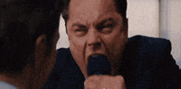 Movie gif. Leonardo DiCaprio as Jordan from Wolf of Wall Street angrily sticks out his jaw, his bottom teeth protruding, as a crowd of men clap his shoulders and encourage him.
