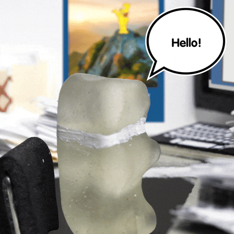 Video gif. Haribo gummy bear with a painted on collar and tie turns away from his computer screen towards us. Speech bubble reads, "Hello!"