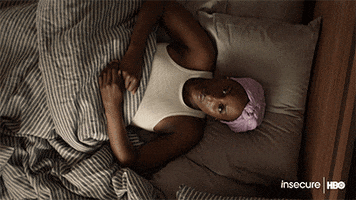 TV gif. Camera rotates and closes in on Issa Rae on Insecure as she lays in bed with a blank expression, thinking.