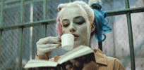 Movie gif. Margot Robbie as Harley Quinn reads a book, while sipping a cup of tea that she holds with her pinky out.
