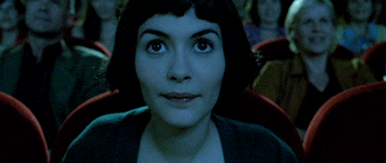 A GIF of a young woman sitting in a dark movie theatre.