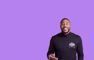 Celebrity gif. Blaise Ffrench stands in front of a purple background and raises one palm. He smiles and says, “Happy Birthday" which appears as text right above his palm. He puts his arm down and the text moves with it.